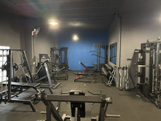 Sala de musculación de Serfit con máquinas de press de pecho, hombro y bíceps en fila, iluminación natural y suelo oscuro